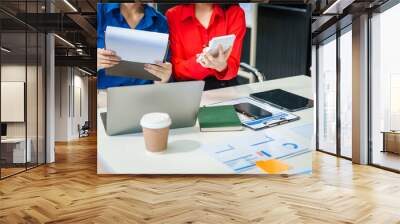 Two young female business consultants work on startup, collaborating on mobile app development social media strategies. whiteboards, documents, they aim to build a successful e-commerce business. Wall mural