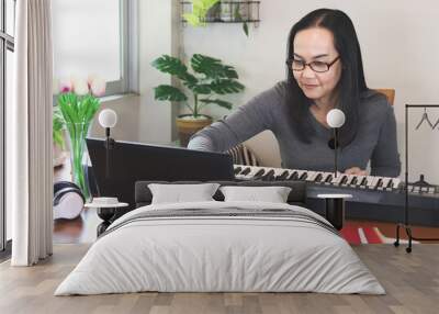 Asian woman learning music lesson online , playing piano and looking at  computer notebook.  Teaching or learning online, social distancing and new normal Wall mural