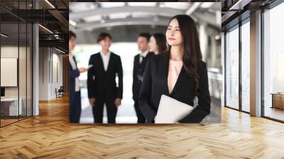 confident beautiful Asian business woman in formal suit holding computer laptop, standing in front of her team, smiling and looking away. Wall mural