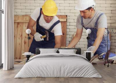 Two Asian repairmen wearing helmet working together in wood workshop , one man nailing plank with hammer Wall mural