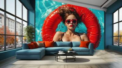 A beautiful young girl in sunglasses on a red inflatable circle in a blue pool. Top view photo Wall mural