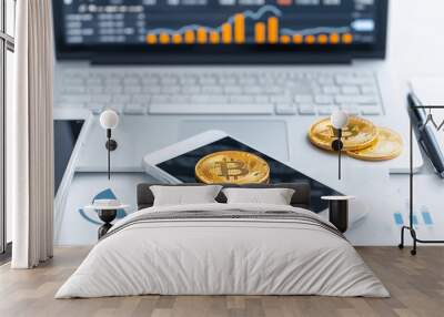 Golden cryptocurrency coins on a smartphone, with financial charts displayed on a laptop in the background, representing digital finance and modern investments. Wall mural