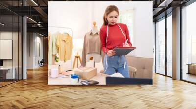 A young woman is holding a tablet and preparing to film content for her online clothing business. She is wearing a red sweater and working in an organized workspace. Wall mural