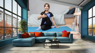 Asian doing home fitness and yoga on a fitness mat doing exercise at modern home in living room, sporty girl health care workout lifestyle and diet concept. Wall mural