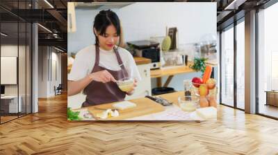 Asian women mixing mayonnaise and chopped boiled eggs for sandwich and dressing for vegetable salad while preparing ingredients for cooking breakfast meal and making healthy food lifestyle in kitchen Wall mural