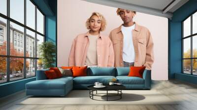 Fashion-forward African American young couple in coordinated pastel jackets posing on a peach background - Concept of modern urban style and partnership Wall mural