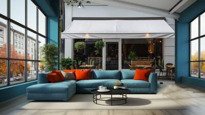 Outdoor seating of a modern cafe with white awning and plants. The cafe storefront features chairs and tables arranged on the sidewalk, creating a cozy and inviting atmosphere in an urban setting. Wall mural