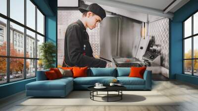 Burger making Food concept Young cook in black uniform is roasting beef for hamburgers on cafes kitchen Wall mural