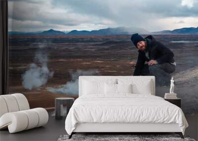 Man feels the warmth of volcanic soil. Hiker places his hand on the ground and feels the geothermal activity of sulphurous heat fumes. Hydrothermal phenomena, cracks in the ground, pleasure. Wall mural