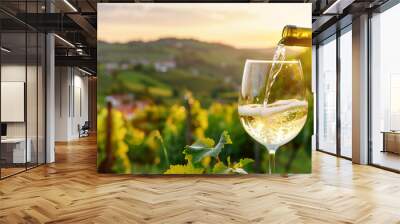  Pouring white wine into glass with vineyard landscape in sunny day Wall mural