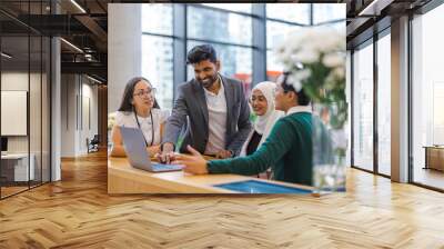 A diverse group of business people gather around a laptop in a modern office
 Wall mural