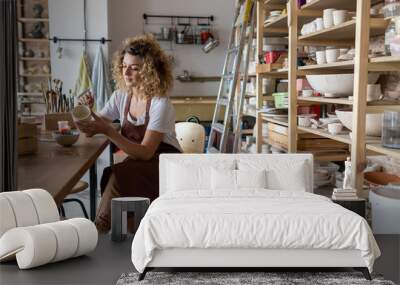 Craftswoman painting a bowl made of clay in art studio Wall mural