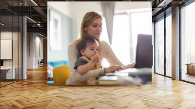 Mother working on laptop with child sitting on her lap 
 Wall mural