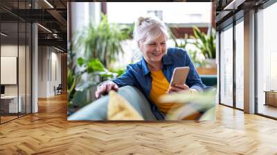 Smiling senior woman using smart phone while sitting on sofa at home
 Wall mural