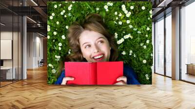 Woman lying on grass, reading book Wall mural