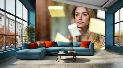 Young businesswoman brainstorming with notes on a glass wall in an office
 Wall mural