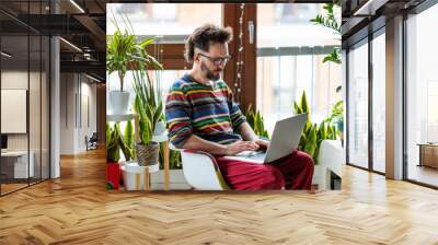 Young man working at home with laptop surrounded by houseplants Wall mural