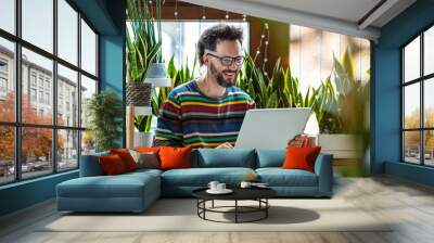 Young man working at home with laptop surrounded by houseplants Wall mural