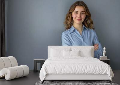 Portrait of a smiling businesswoman in a blue shirt and grey skirt standing with arms crossed isolated on a gray background, copy space concept for your design—a smiling female employee or manager.  Wall mural