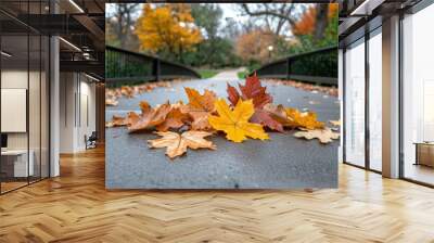 A vibrant collection of yellow, orange, and red autumn leaves rests on a peaceful bridge pathway. The crisp air and soft light create a serene atmosphere, perfect for a tranquil nature walk. Wall mural