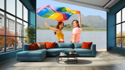 young lesbian couple beautiful friends standing and waving rainbow flags for celebrating equality sexual freedom, LGBT people enjoy outdoor activities at nature park during summer day in pride month Wall mural