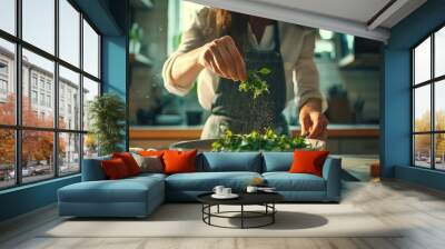 A woman in an apron adds fresh herbs to a bowl of greens, creating a vibrant and healthy salad in a bright kitchen. Wall mural