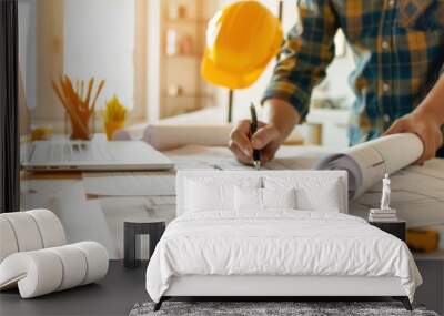 Architect at work with architectural plans and a laptop. A hard hat and stationery are on the table, indicating a construction environment. Wall mural