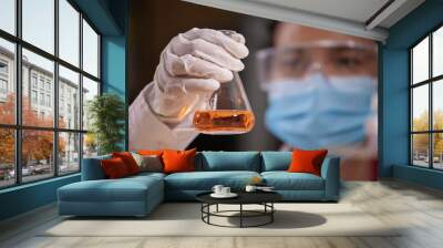 Asian scientist is holding a test tube with orange liquid chemical for analysis and research chemical test in a laboratory. Wall mural