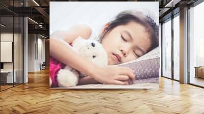 Cute asian child girl sleeping and hugging her teddy bear in the bed Wall mural