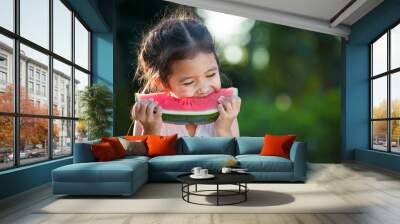 Cute asian little child girl eating watermelon fresh fruit in the garden Wall mural