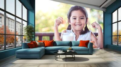 Cute asian little child girl making strong hand while drinking a milk for breakfast with fun Wall mural