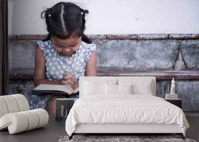 Cute asian little girl closed her eyes and  folded her hand in prayer on a Holy Bible for faith concept in vintage color tone Wall mural