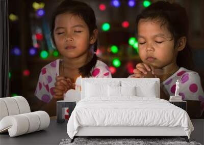 Happy twin two asian little girls make folded hand to wish the good things for their birthday in birthday party in dark tone Wall mural