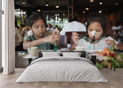 Two asian child girls eating delicious fried fish and salad in the restaurant with family. Wall mural