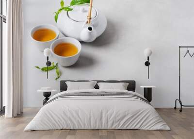 Tea concept with white tea set of cups and teapot surrounded with fresh tea leaves on concrete background with copy space. Wall mural