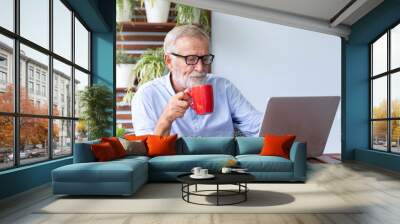 Senior retirement man is working with his laptop at home with a cup of coffee Wall mural