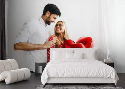 Couple. Love. Valentine's day. Emotions. Man and woman are looking at each other and smiling, she is holding red heart-shaped balloons Wall mural