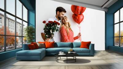 Couple. Love. Valentine's day. Emotions. Man is giving heart-shaped balloons to his woman, both smiling; on a white background Wall mural