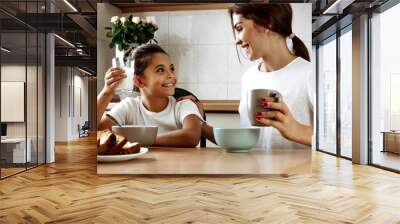 Family. Eating. Home. Mom and daughter are talking and smiling while having lunch in the kitchen at home Wall mural