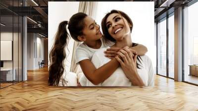 Family. Love. Mom and daughter are hugging, looking at each other and smiling while sitting on couch at home Wall mural