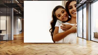 Family. Love. Togetherness. Portrait of happy mom and daughter hugging, looking at camera and smiling; at home Wall mural