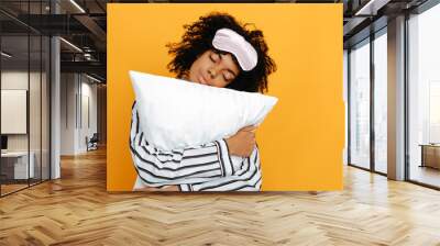 Sleeping. Dreams. Woman portrait. Afro American girl in pajama is hugging a pillow, on a yellow background Wall mural