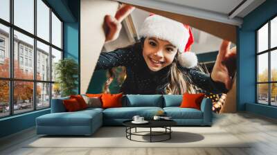 Surprised cute child girl opening a Christmas present. Little kid having fun near decorated tree indoors.  Happy  holidays and New Year. Wall mural