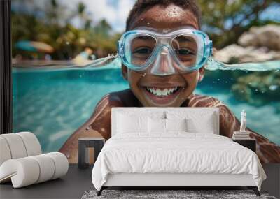 A cheerful young swimmer wearing goggles is smiling in the clear water of a swimming pool, enjoying a sunny day with other swimmers in the background. Wall mural