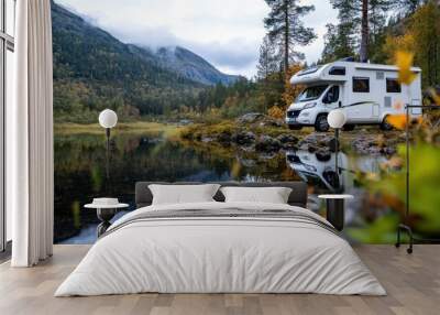 A recreational vehicle is parked by a serene lake, surrounded by autumn foliage and mountains in the background, capturing a peaceful and adventurous outdoor setting. Wall mural