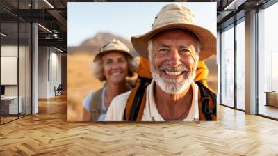 A senior couple smiles while hiking in a desert landscape, equipped with backpacks and hats, showcasing their adventurous spirit and love for outdoor activities and exploration. Wall mural