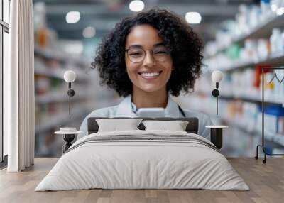 A smiling pharmacist with curly hair and glasses stands in a pharmacy, using a smartphone, symbolizing modernity and customer engagement in healthcare services. Wall mural