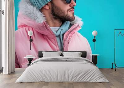 A stylish man wears a pink jacket and blue beanie, presenting a modern and fashionable look against a vibrant blue background, showcasing contemporary fashion trends. Wall mural