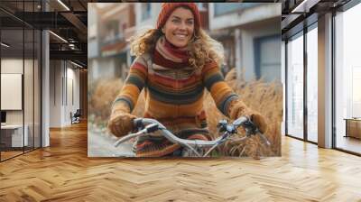 A stylish woman glides through the outdoor scenery, her scarf fluttering in the wind as she confidently rides her bike past a beautiful building, her determined expression showing her love for both f Wall mural