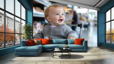 A thrilled baby, wearing a cozy sweater, is having fun seated in a shopping cart inside a grocery store, surrounded by various products, with an infectious smile. Wall mural